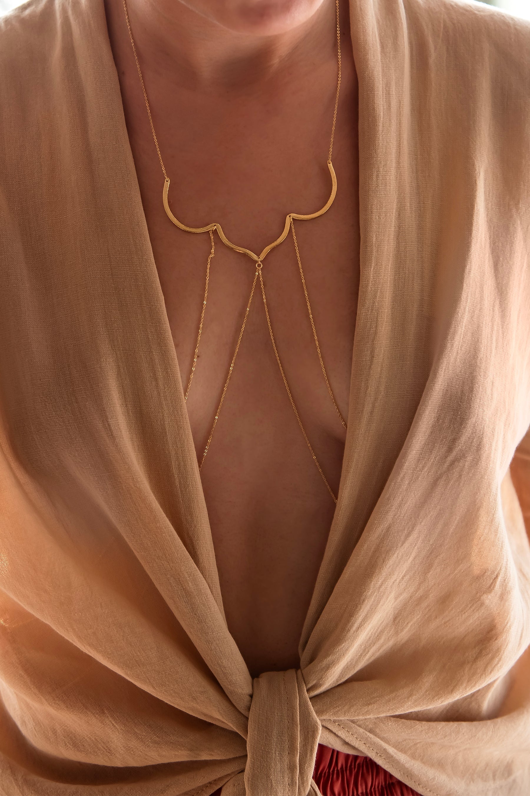 Person wearing a beige top with a gold necklace, blurred background