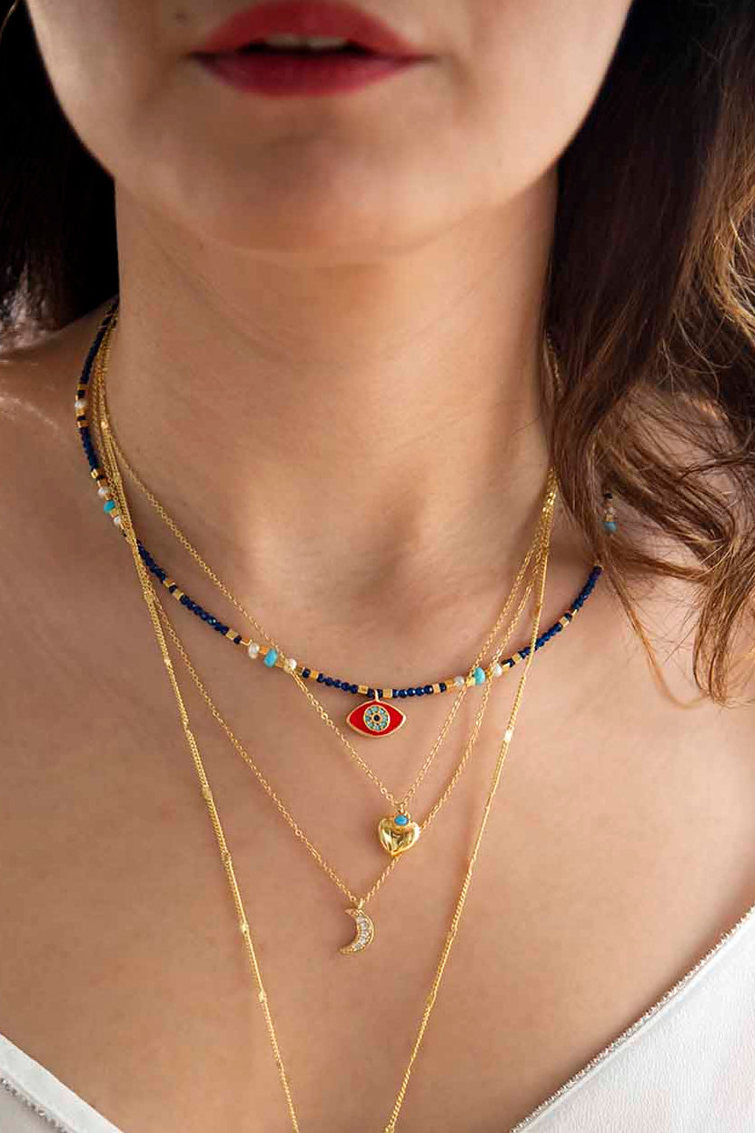 Close-up of a woman wearing multiple necklaces with a focus on a gold necklace with a red pendant.