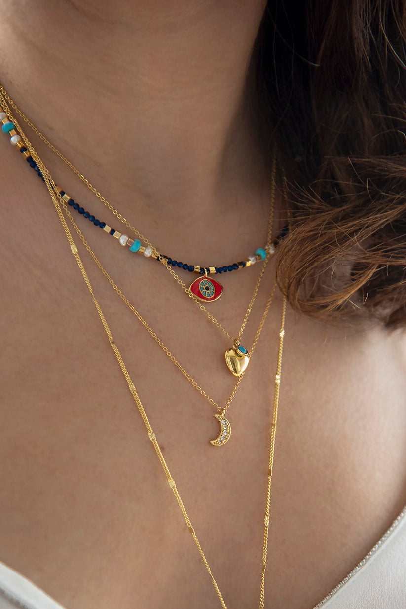 Close-up of a person wearing multiple necklaces with various pendants on a blurred background