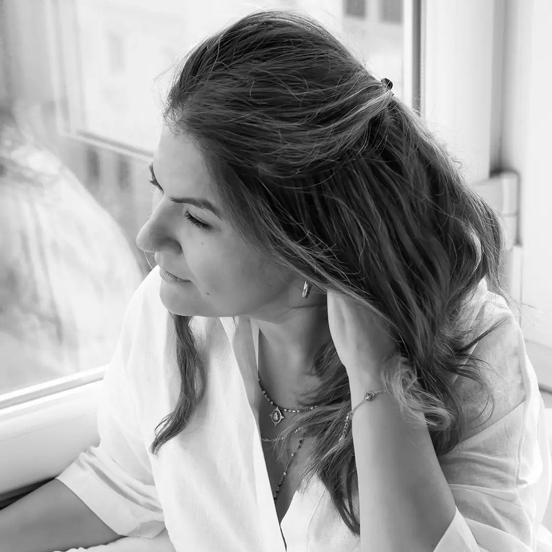 Woman in a white robe sitting on a couch, looking out of a window.