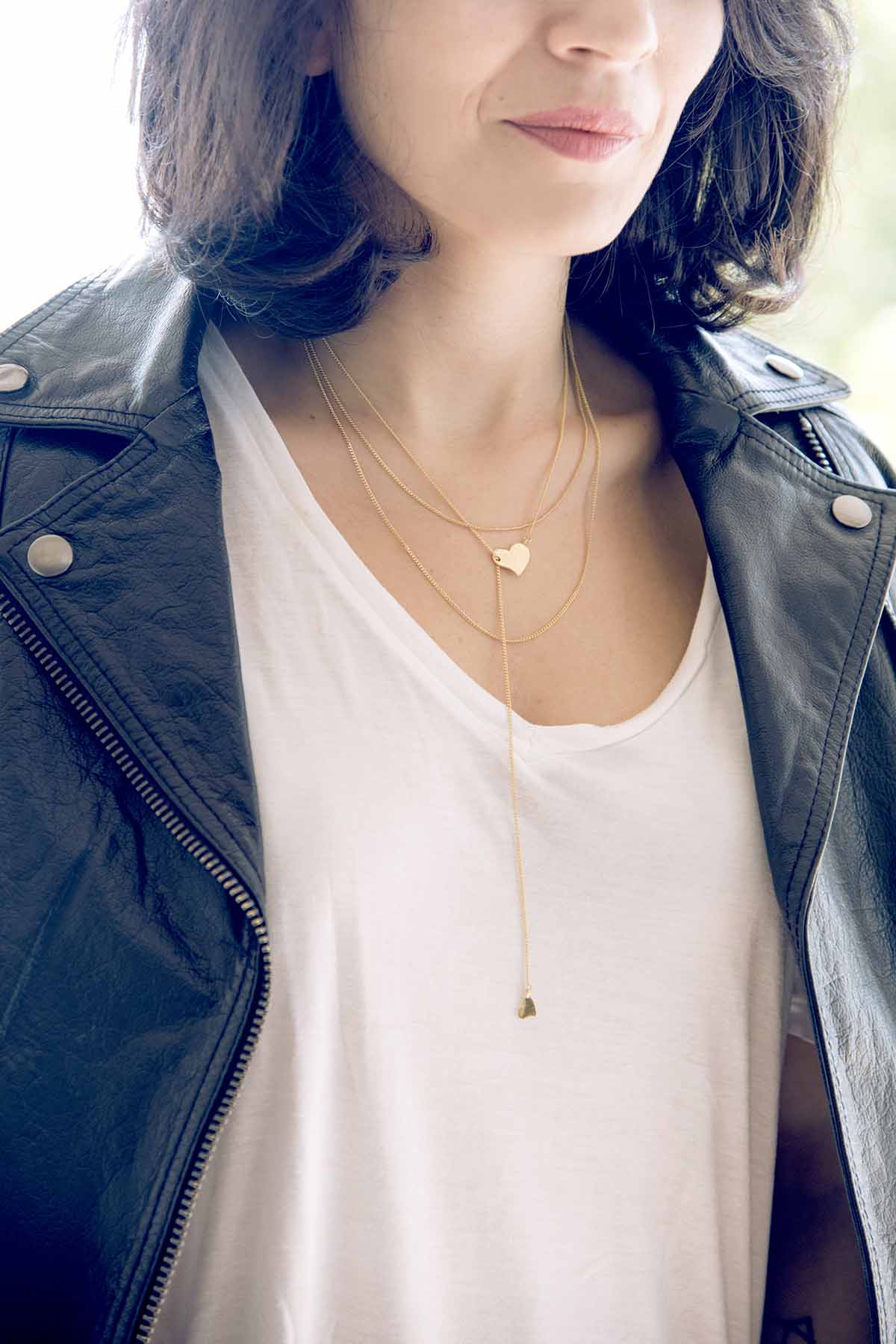 Person wearing a black leather jacket and white top with a gold necklace featuring a heart pendant.