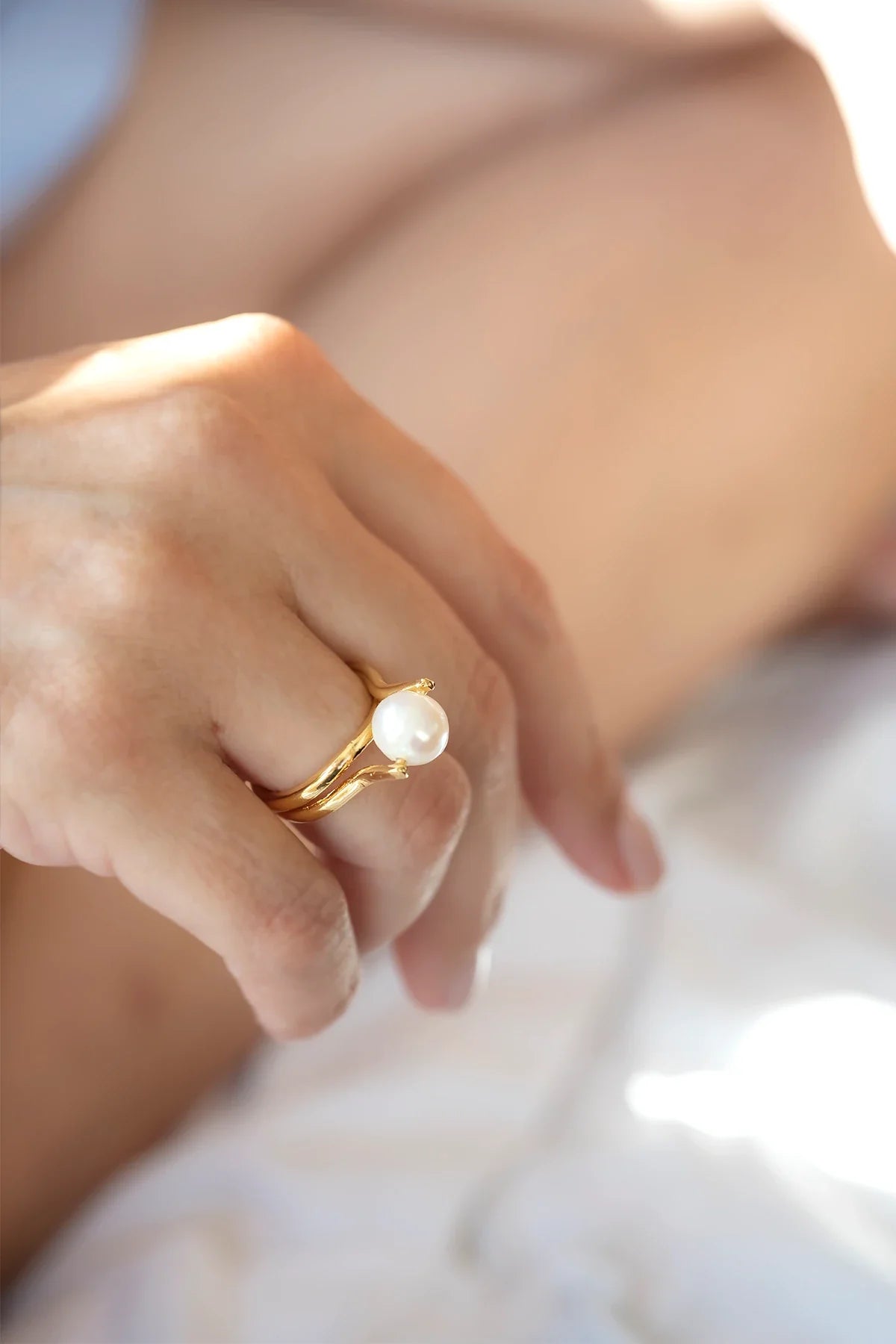 Close-up of a hand wearing a gold ring with a pearl on a blurred background
